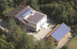 Das Gebäude Büschiheim in Köniz/BE. Links im Bild ist die teilweise aufgeständerten 39 m2 grosse Sonnenkollektoranlage, auf dem Flachdach die aufgeständerte PV-Anlage Büschi II mit 5.4 kWp zu sehen,  und rechts im Bild ist die sorgfältig ganzflächig integrierte PV-Anlage Büschi I mit 10.4 kWp.